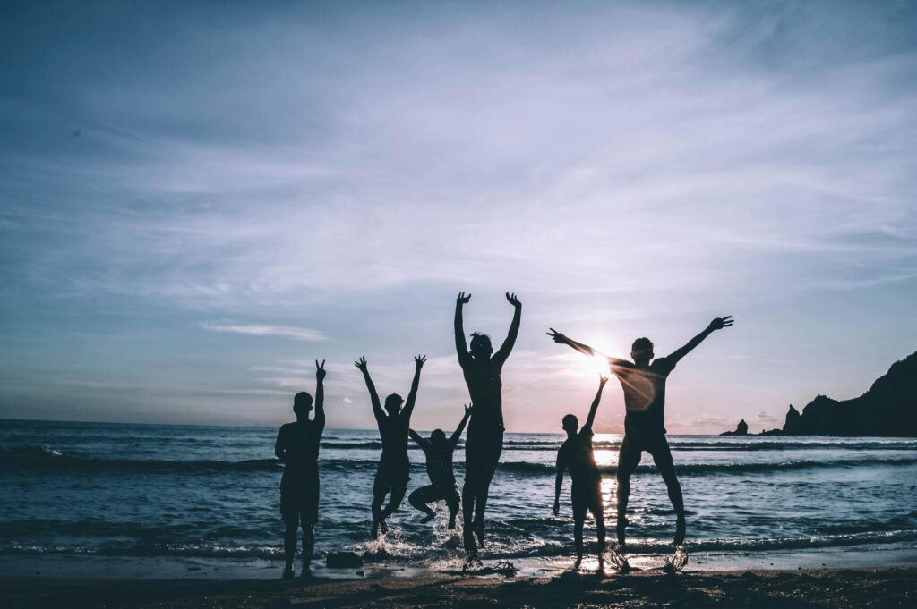 Silhouetted group of friends jumping joyfully on the beach at sunset, symbolizing freedom and happiness.