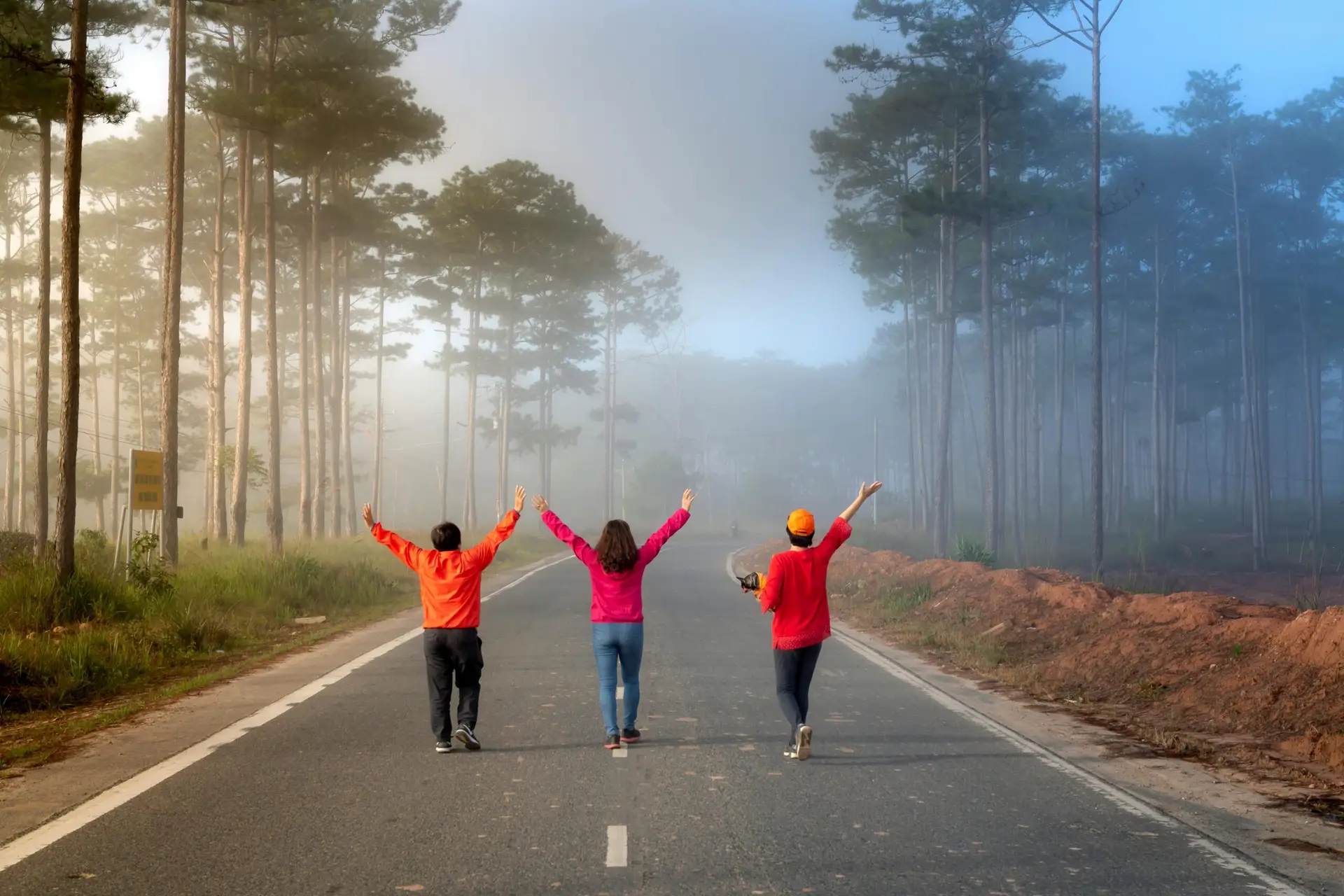 Three people walk arm-in-arm on a foggy forest road, creating a serene and joyful mood.