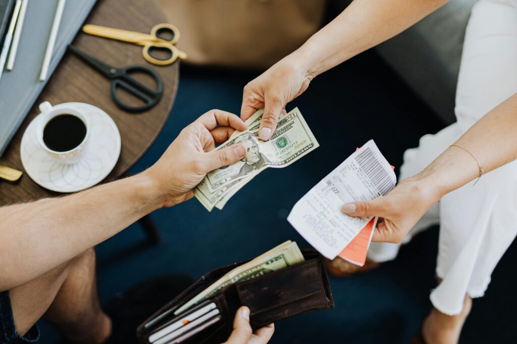 Close-up of a transaction with US dollar bills and receipts being exchanged over a table with coffee and scissors.