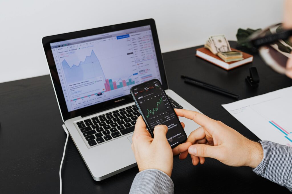 Person analyzing stock market data on a laptop and smartphone indoors.