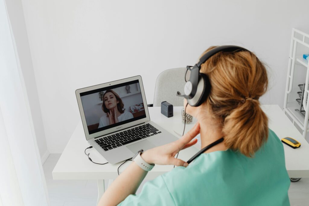 Woman in medical scrubs having a telemedicine session using a laptop from home.