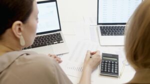 Two people analyzing business data on laptops with charts and graphs.