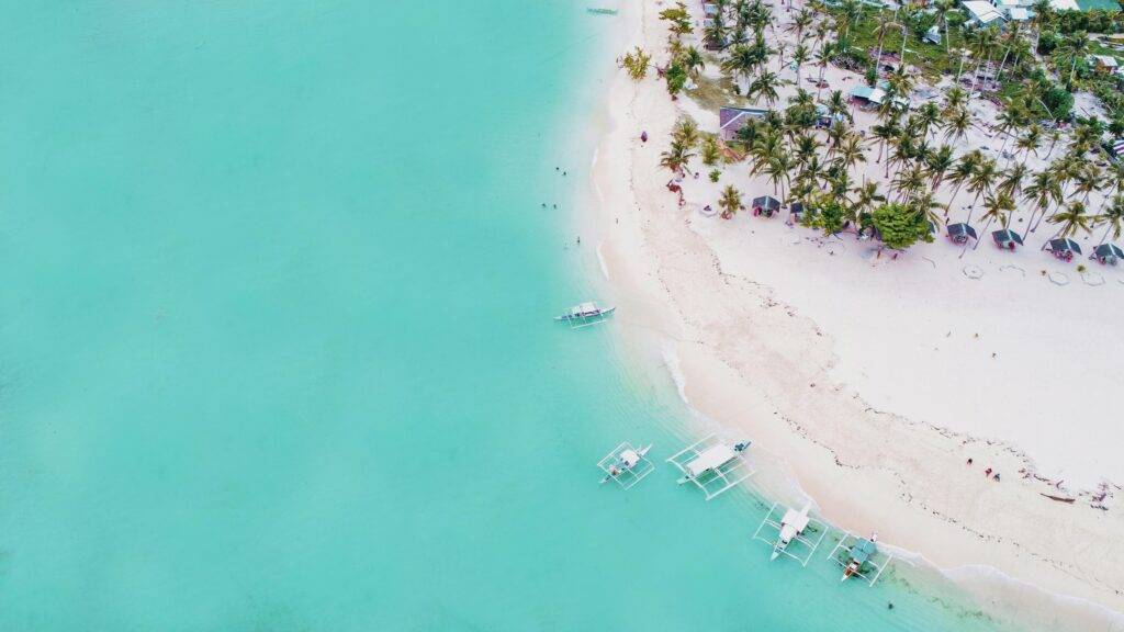 Aerial view of a serene tropical beach with turquoise water and palm-lined shores.