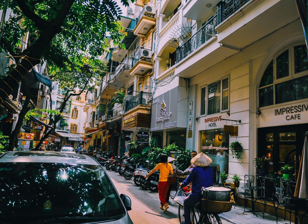 Vibrant street life in Hanoi with locals, cafes, and motorbikes on a sunny day.