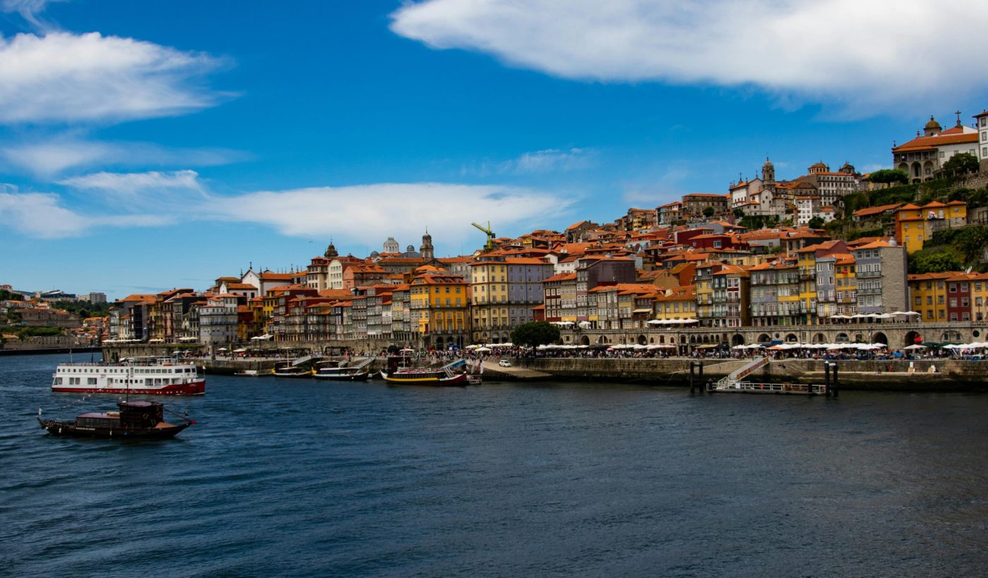 Beautiful panoramic view of Porto's riverside with colorful buildings and boats under a vibrant blue sky.