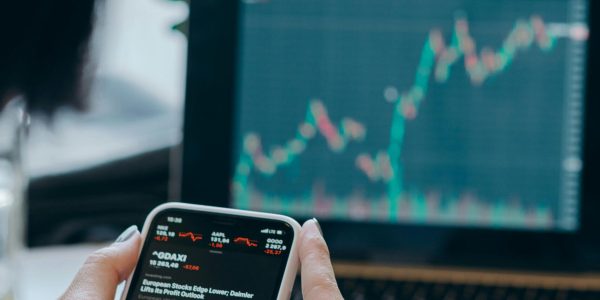 Person using smartphone for stock market analysis at home office.